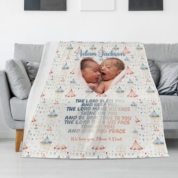 A cozy living room features a Personalized Baby Name Blanket elegantly draped over a couch. The custom photo blanket showcases images of two smiling babies accompanied by a blessing in beautiful decorative script, all surrounded by gentle pastel patterns. The personalized message reads, "We love you, Mom & Dad.