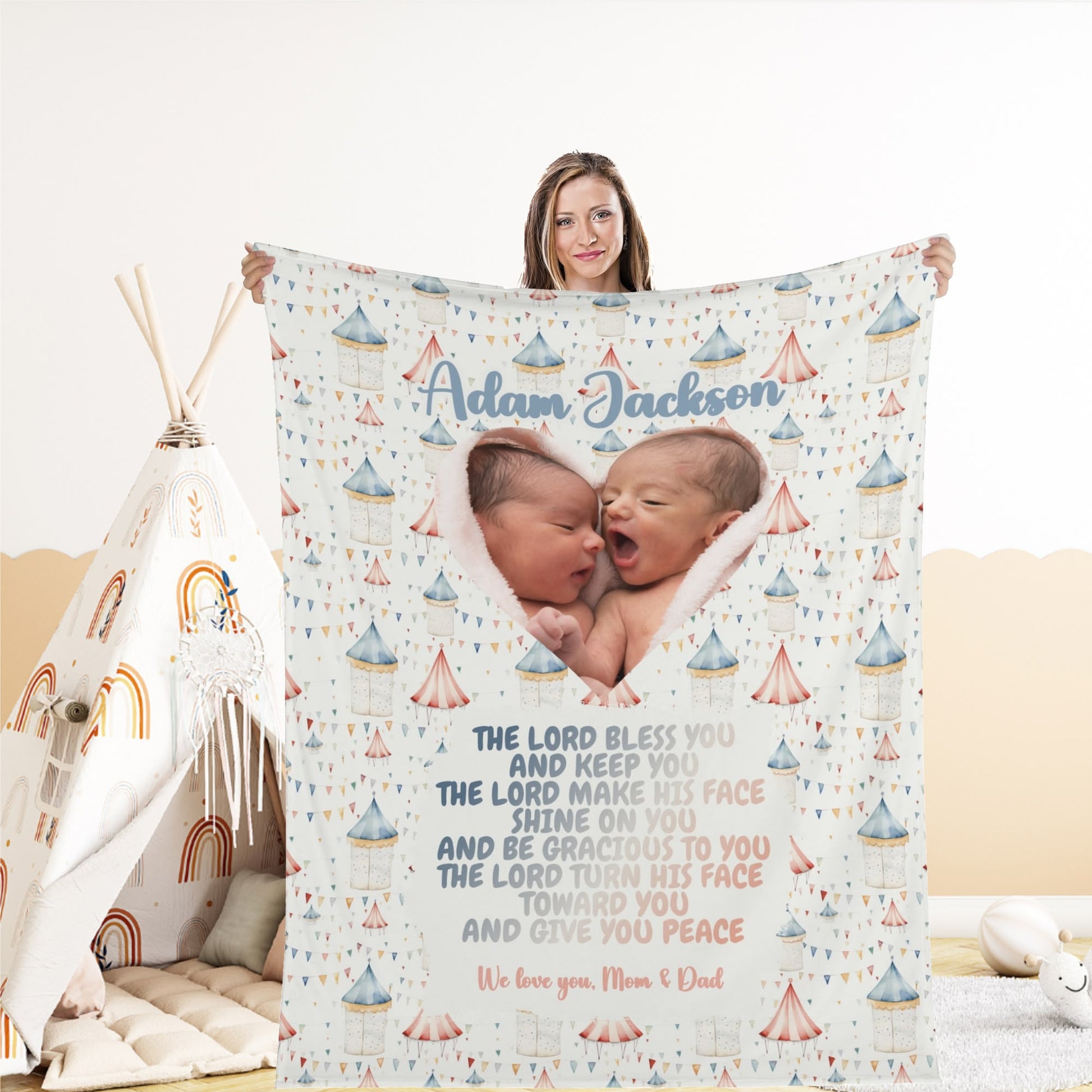 A woman beams as she holds a Personalized Baby Name Blanket, featuring an image of two newborns and a whimsical design with tents and rainbows. The customized text includes the name "Adam Jackson" alongside a heartfelt blessing.