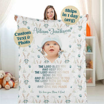 A woman holds a Personalized Baby Name Blanket, custom-designed with woodland creatures and a photo of a baby. The blanket includes a Bible verse and offers customizable options for text or photos. A bubble indicates "Ships in 1 day (avg.)" Baby toys are visible in the background, making it an ideal personalized gift for newborns.