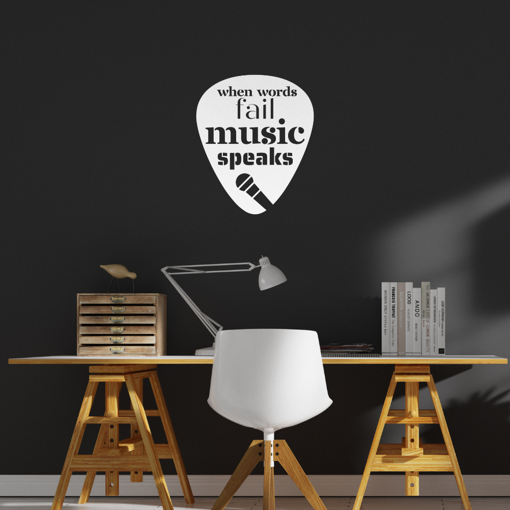 A modern desk featuring a white chair and lamp is set against a black wall, accented by the stylish "When Words Fail, Music Speaks | Mic" sign crafted from powder-coated metal in the shape of a guitar pick. This charming piece adds character to your home decor with its musical theme and microphone icon.