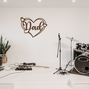 A stage featuring a drum set, microphones, guitar, and pedals. On the white wall hangs the Dad Heart Sign | Metal Wall Art, while a potted plant in a basket adds charm—ideal for rehearsal spaces or as a unique gift for Dad.