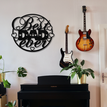 A wall displays the Best Dad Circle Sign | Metal Wall Art, with two electric guitars hanging nearby and a Yamaha piano below, surrounded by potted plants.