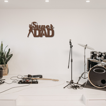 A music stage with drums, mics, and guitar gear showcases a large Super Guitarist Dad Sign | Metal Wall Art—an ideal gift for music lovers. A potted plant adds extra charm to the setup.
