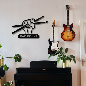 A room with a black Yamaha piano, potted plants, two electric guitars on the wall, and the Dad Rocks Sign with Hand and Drumsticks | Metal Wall Art makes the perfect gift space for dad.