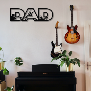 A room with a Yamaha piano, two potted plants, guitars on the wall, and a "Dad Text Sign with Drummer Figures | Metal Wall Art" above—an ideal unique gift for drummer dads.