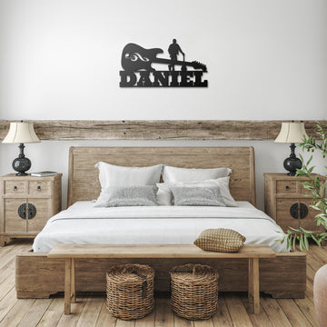 A rustic bedroom has a wooden bed with white bedding, bedside tables with lamps, a bench with wicker baskets, and above the bed, custom metal wall art: the "Electric Guitar with Guitarist Wall Sign Custom Name.