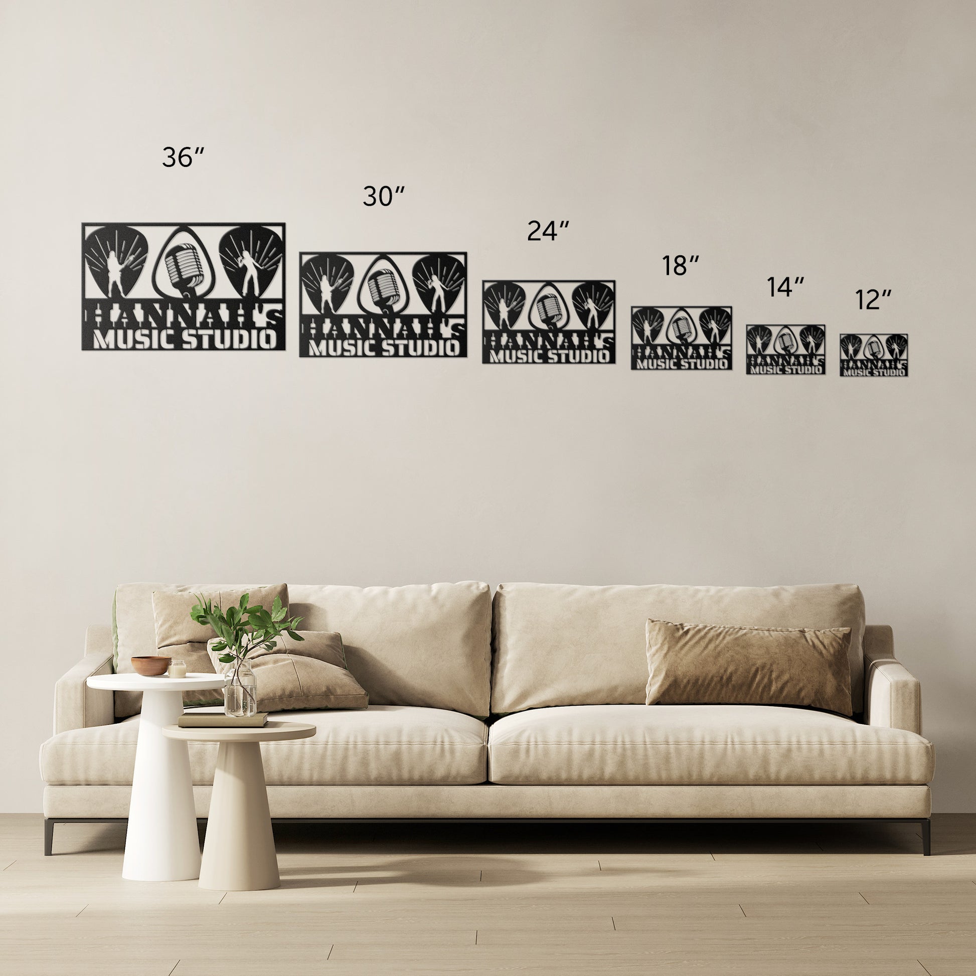 A beige sofa with two cushions sits against a light wall. Above, six black "Guitarist Singer Wall Sign Custom Name" metal arts (12"–36") add unique decor. A small round table beside the sofa holds a vase and a book.