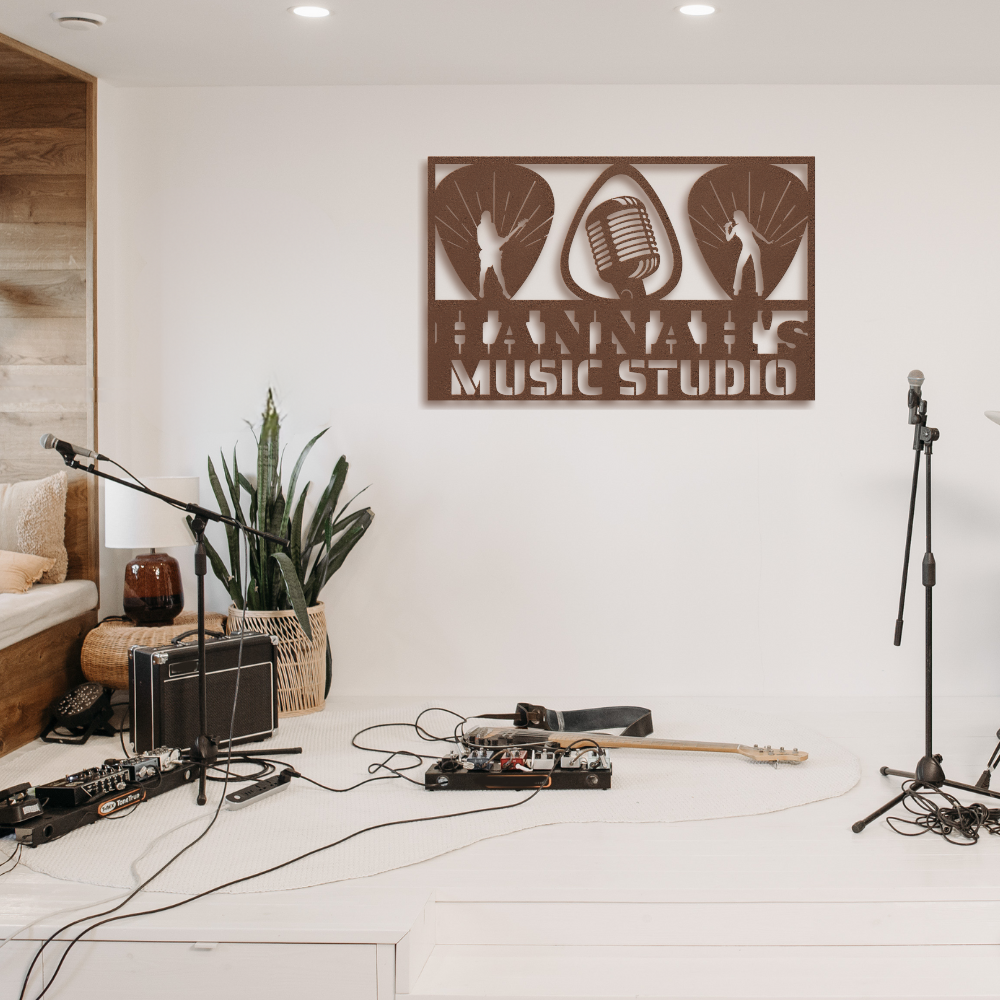 A stylish home music studio setup features a Guitarist Singer Wall Sign Custom Name | Custom Metal Wall Art above plants, microphones, a guitar, speakers, and cables on a white floor with a cozy seating area for modern decor.