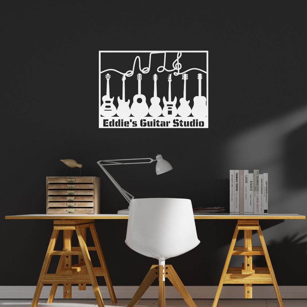 A modern workspace with a white chair and desk against a dark wall is accented by the Multiple Guitars Wall Sign with Music Notes and Custom Text, an 18 gauge steel art piece reading "Eddie's Guitar Studio.