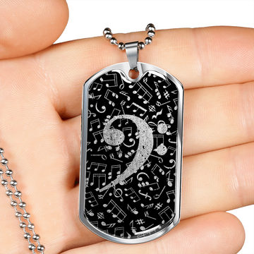 A hand holds the Dog Tag Necklace Black, featuring a bass clef cutout and distressed music notes—a unique personalized gift for musicians.