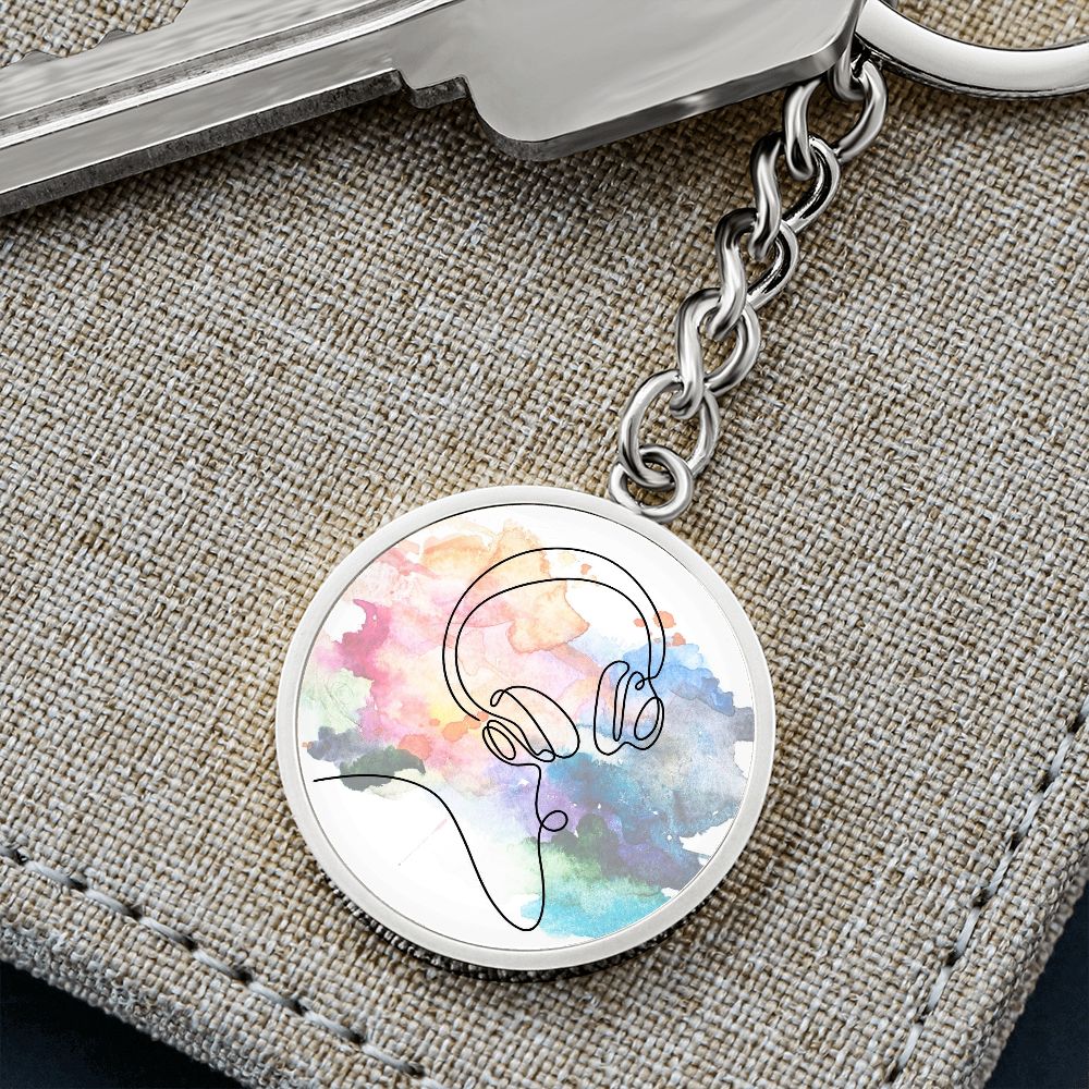 The Head Phones Colorful Circle Pendant Keychain features a line drawing of headphones over a vibrant watercolor background—an ideal, personalized gift for any music lover.