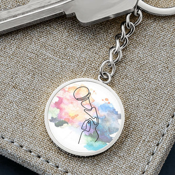 A round metal keychain named "Microphone Colorful | Circle Pendant Keychain | Gift for Singer" features vibrant art of a microphone and sits on a textured beige surface beside a silver key.