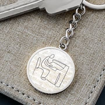 The Piano Sheet Music Circle Pendant Keychain features a minimalist design of a person playing piano over faint sheet musicβan engraved silver keychain, perfect as a unique gift for any pianist or music lover.