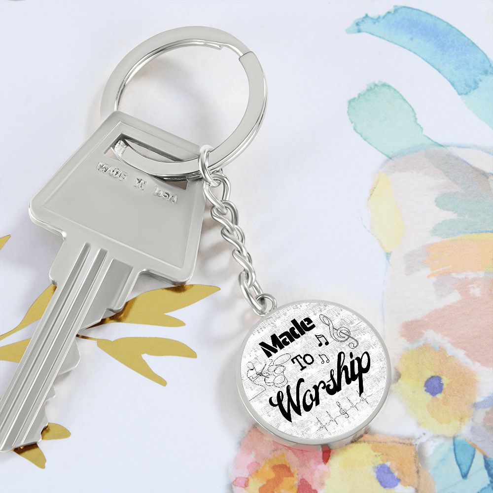 A silver key with a round keychain reading "Made to Worship" and sheet music with drums, set on a vibrant floral background—an ideal Made to Worship Silver Sheet Music gift for drummers.