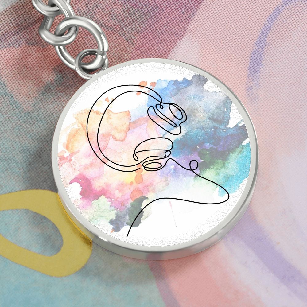 A round pendant keychain featuring a colorful headphone design, perfect as a personalized gift for music lovers. Presented with an abstract pastel background for a unique touch.