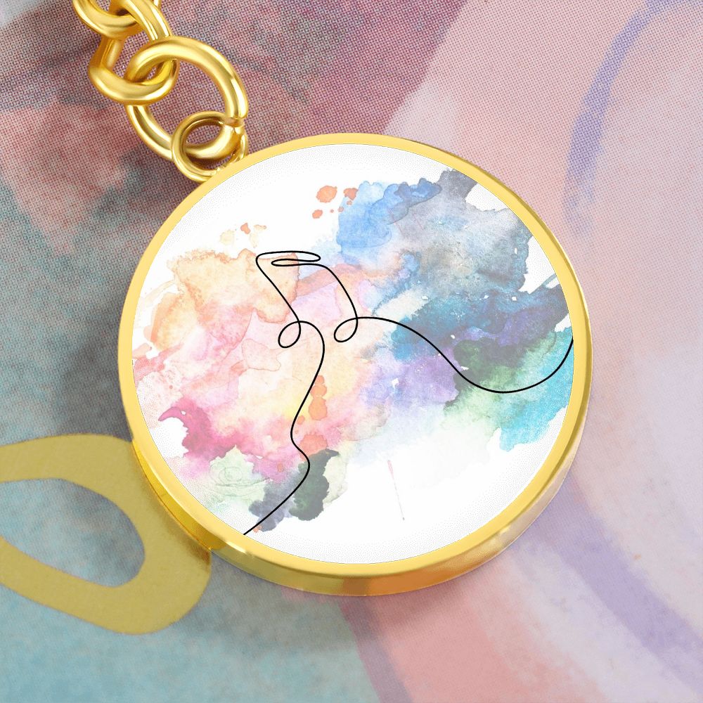 The "Music Notes Colorful" circle pendant keychain features a gold finish and vibrant watercolor background with minimalist music notes, making it a perfect gift for musicians. The engraved keychain rests on a matching watercolor-patterned surface.