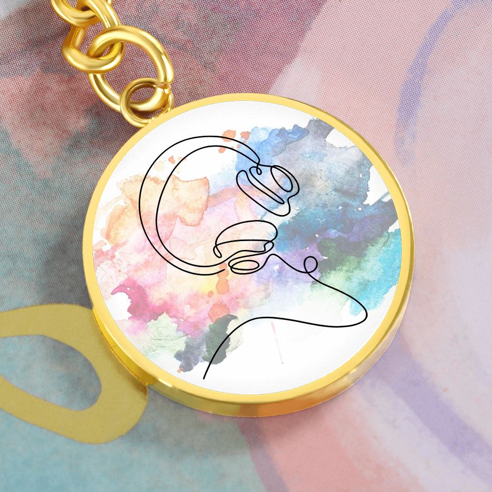 A round pendant keychain featuring colorful headphones and a minimalist line drawing makes a unique personalized gift for music lovers, resting on an abstract pastel surface.