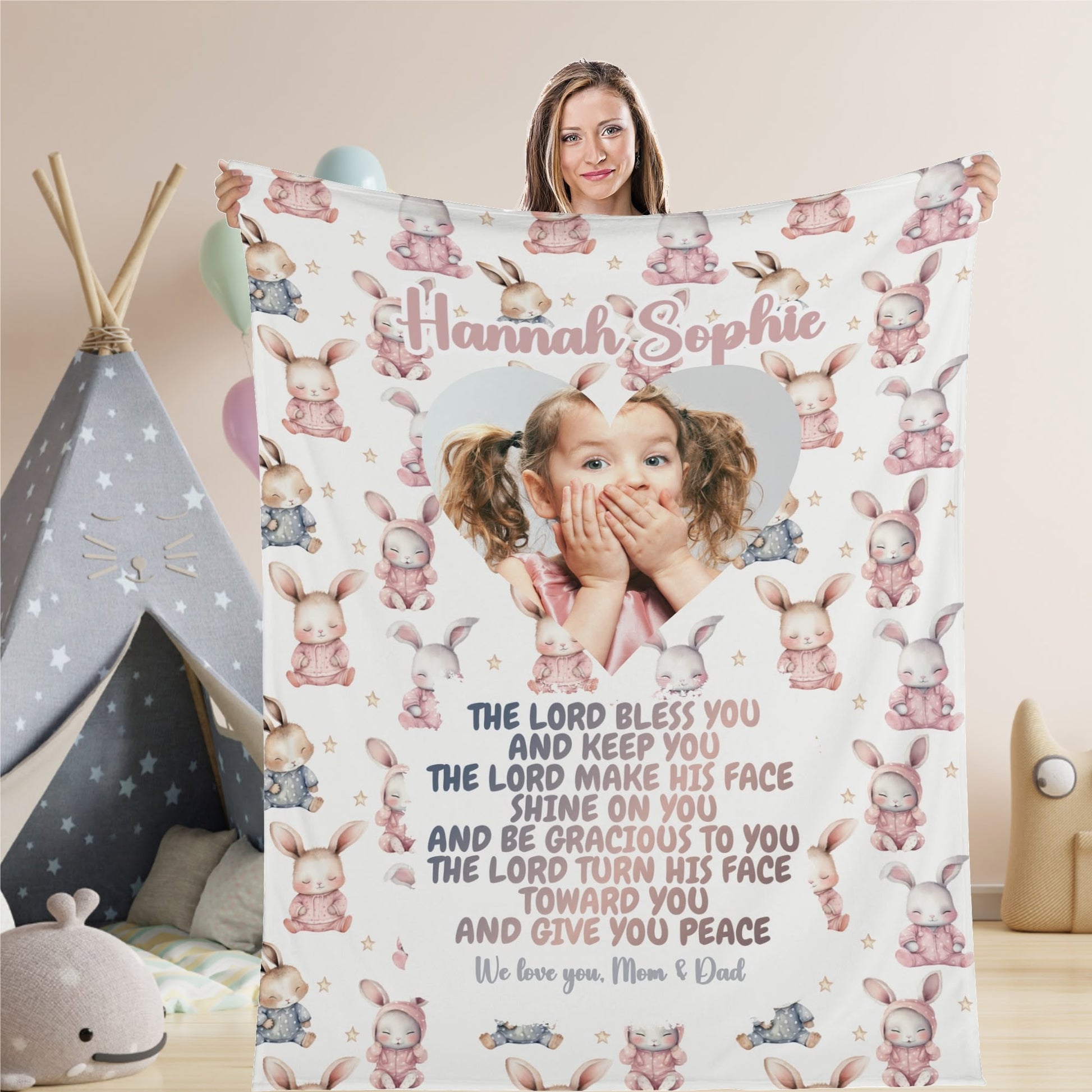 A woman holds a Personalized Baby Name Blanket featuring a custom photo of a young girl within a heart shape. With charming bunny illustrations, it carries the heartfelt message: "We love you, Mom & Dad.