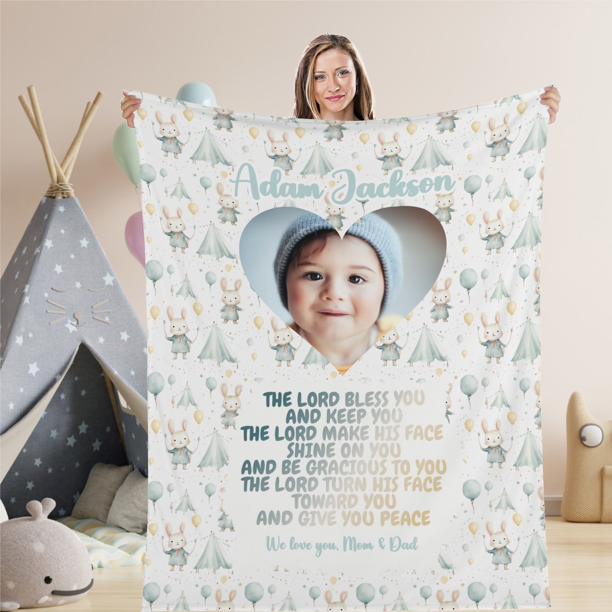 A woman holds a Personalized Baby Name Blanket, featuring a heart-shaped photo of a beanie-wearing baby. The soft pastel designs of tents, trees, and balloons adorn the blanket alongside a touching blessing and the words "We love you, Mom & Dad," making it the perfect custom photo blanket gift for any occasion.