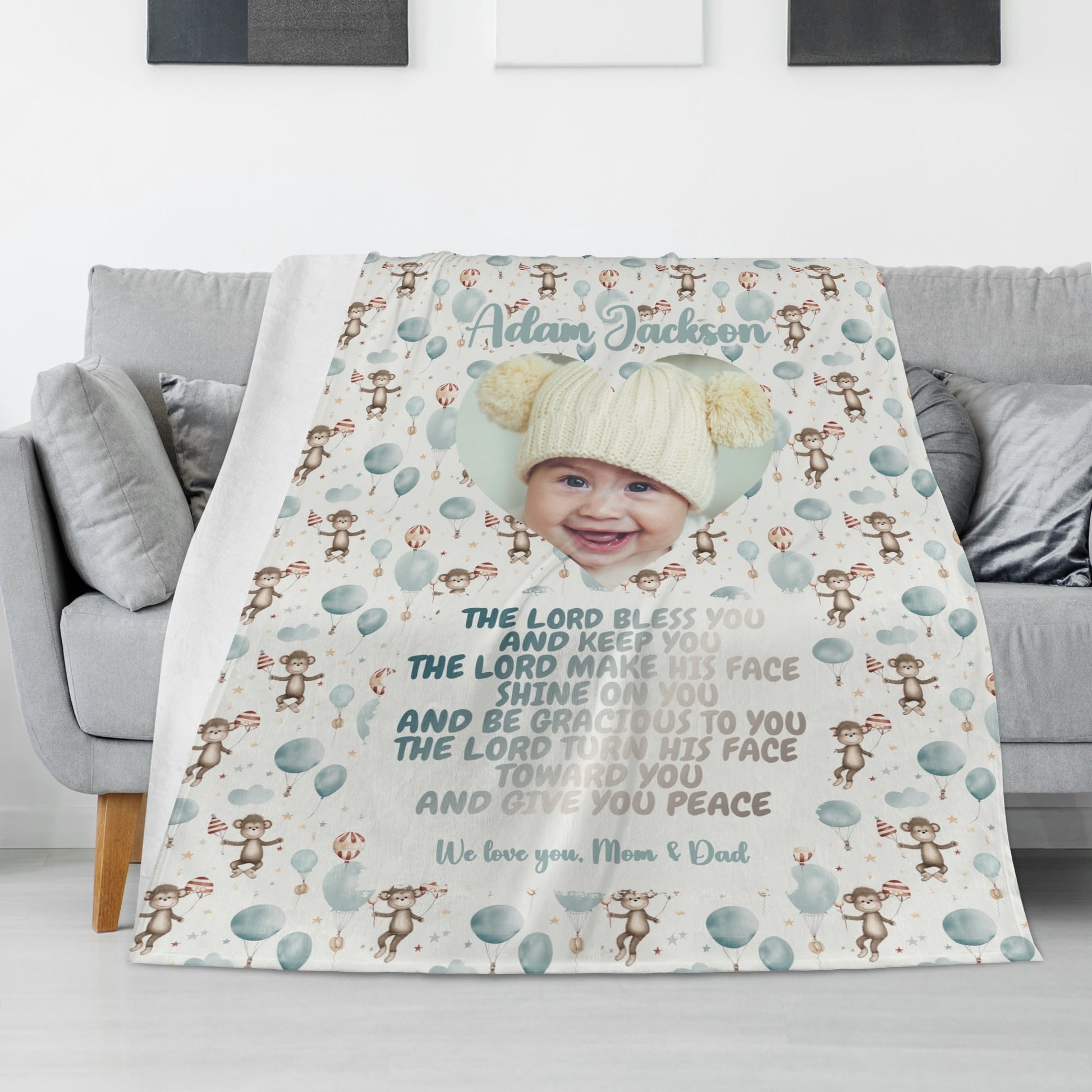 A Personalized Baby Name Blanket artfully drapes over a sofa, showcasing a baby's photo at its center. Decorated with monkeys, balloons, and heartfelt messages from Mom and Dad, this Custom Photo Blanket Gift includes a cherished blessing to treasure forever.