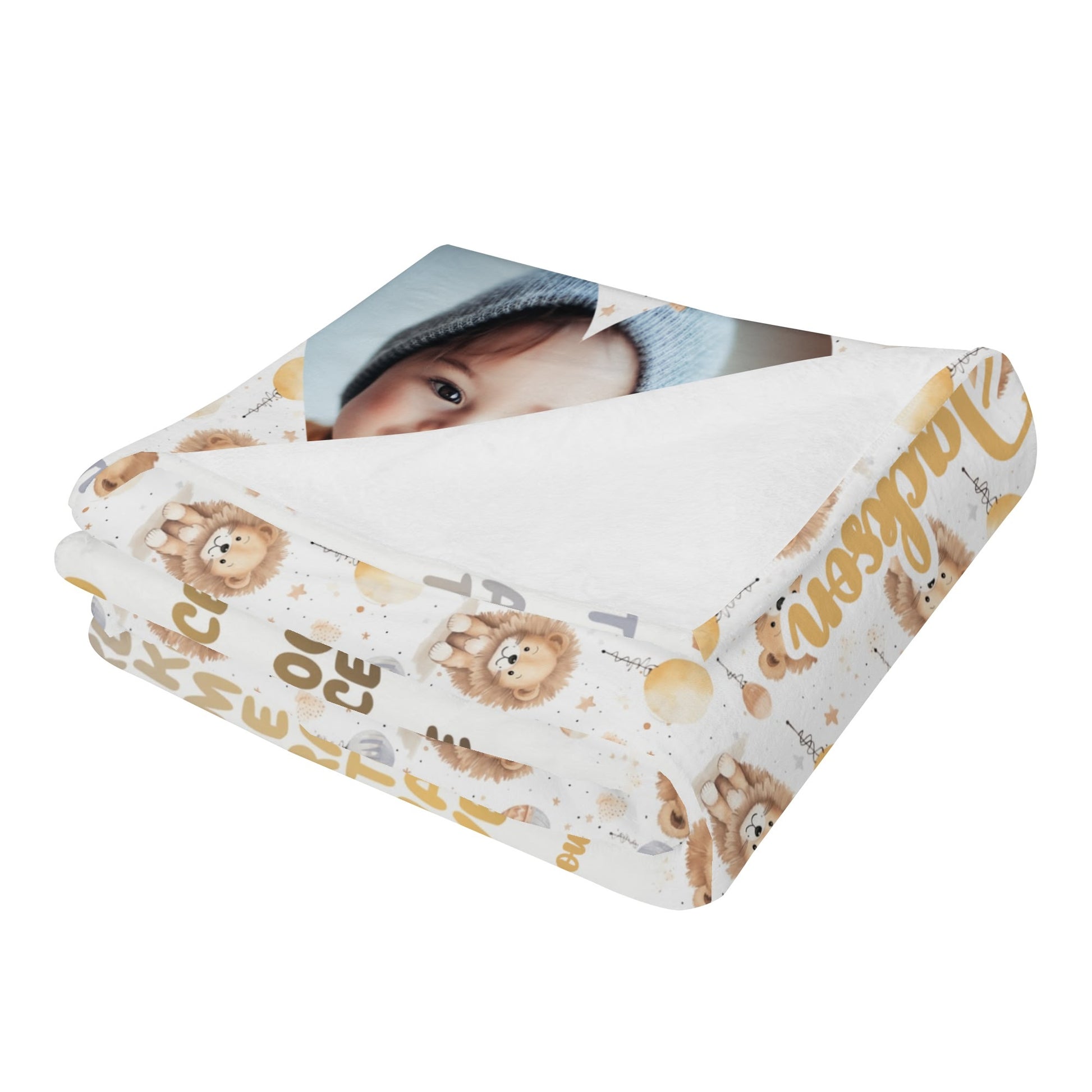 A folded personalized baby name blanket showcases teddy bears and alphabet letters, with a portion of a baby photo gently tucked under the corner. Crafted in elegant gold and brown tones, it transforms into a cherished keepsake when embellished with custom text or a heartfelt baby blessing.