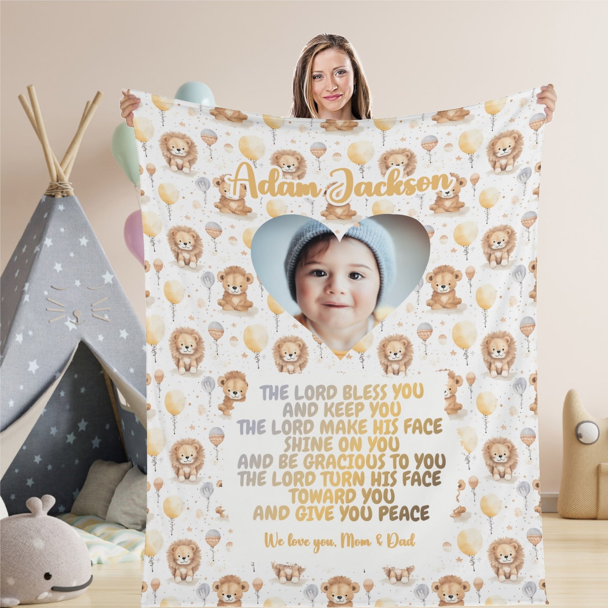 A woman holds a Personalized Baby Name Blanket from the baby blessing collection. This customized photo blanket, adorned with lion and balloon designs, features a heart-shaped image of a baby along with the Bible verse: "The Lord bless you and keep you..." and the personalized text: "We love you, Mom & Dad.