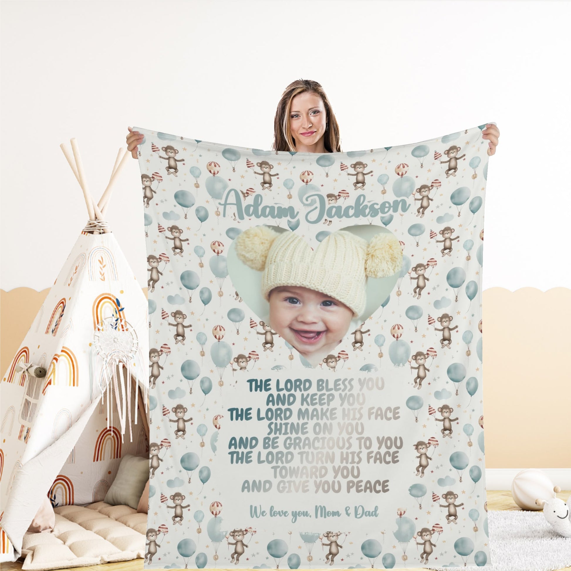 A person holds a Personalized Baby Name Blanket, customized with a photo of a baby wearing a knitted hat. The blanket is decorated with balloons and teddy bears and features personalized text concluding with "We love you, Mom & Dad.