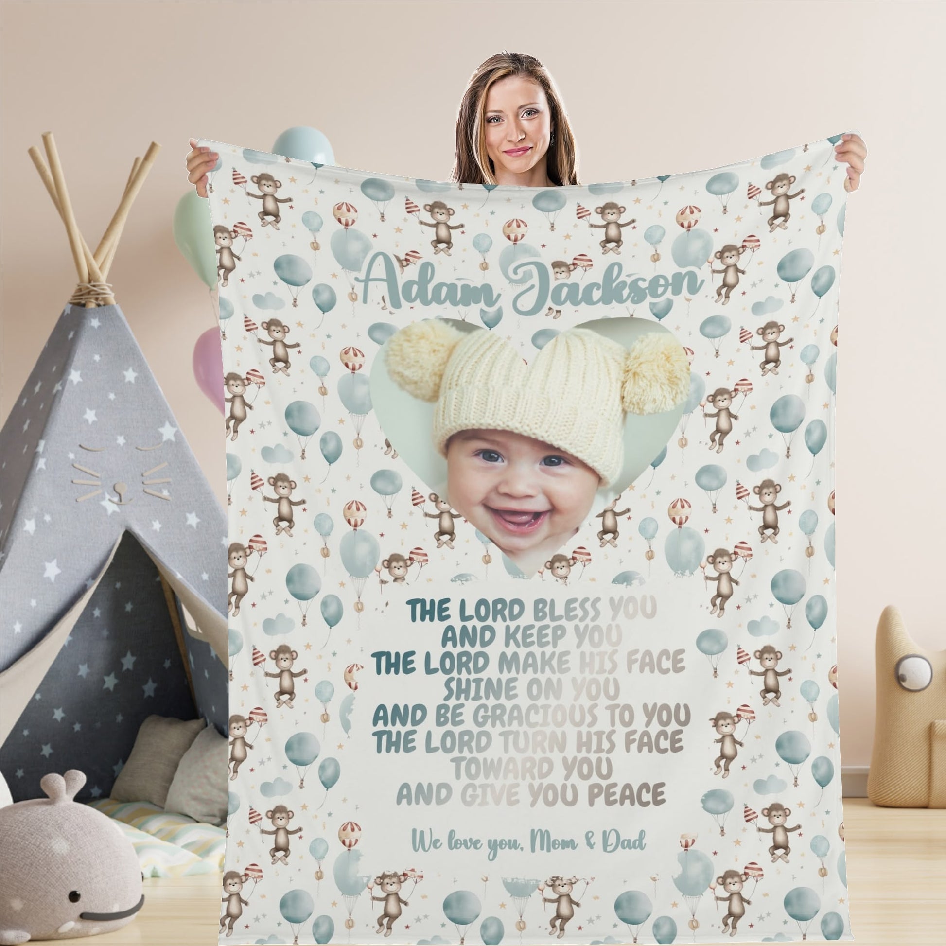 A woman proudly displays a Personalized Baby Name Blanket, a Custom Photo Blanket Gift showcasing a child's image within a heart. Adorned with cheerful cartoon monkeys and balloons, it features the name "Adam Jackson" along with the beginning of a Bible verse: "The Lord bless you and keep you.