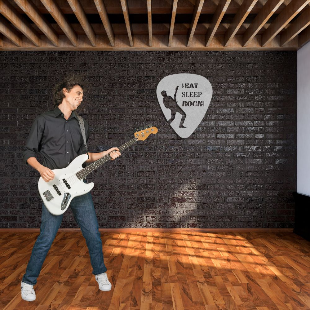 A man playing an electric guitar stands on a wooden floor against a black brick wall. Above him, a metal wall sign shaped like a guitar pick and inscribed with "Eat, Sleep, Rock, Repeat" adds flair to the scene. Sunlight streams through the window, casting patterns on the floor.