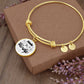 A Personalized Made to Worship Drums Round Pendant Bangle – Silver Sheet Music rests on a brown box, surrounded by purple flowers. The main round pendant features the inspiring phrase “March to the beat of your own drum” with floral accents—making it a meaningful personalized gift for drummers, ideal for worship team appreciation.