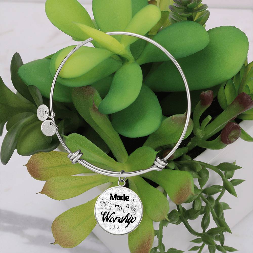 A Personalized Made to Worship Drums Round Pendant Bangle – Silver Sheet Music, featuring a round charm inscribed with “Made to Worship,” hangs on a vibrant green succulent in a white pot—a meaningful worship team appreciation or personalized gift for any Christian drummer’s bangle collection.