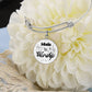 The Personalized Made to Worship Drums Round Pendant Bangle – Silver Sheet Music rests on a large, light-colored flower. This silver bracelet features a round charm inscribed with “Made to Worship,” surrounded by music notes and a treble clef, making it a thoughtful worship team appreciation or personalized drummer gift.