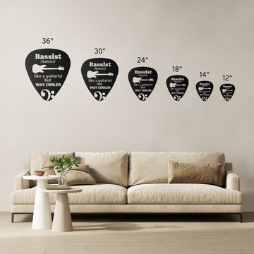 Six black guitar pick-shaped wall decals, each in a different size and featuring humorous bassist and guitarist quotes, are displayed above a beige sofa. In front of the sofa, round coffee tables and decorative items create a playful setting that pairs perfectly with the Pick Sign with Bassist Definition | Metal Wall Art or other guitar-themed accents.