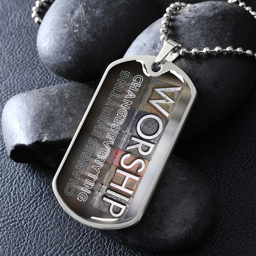 Silver military-inspired dog tag pendant with bold vertical worship typography and “Worship Changes Everything” for a worshipper, beside black stones