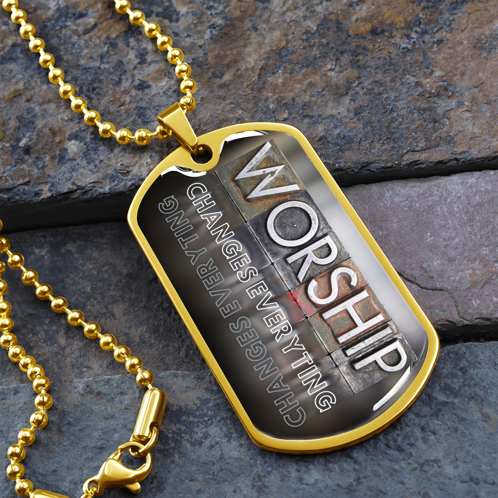 Gold-finish worship dog tag necklace featuring bold vertical worship typography and “Worship Changes Everything” on stone